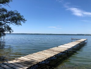 Une jetée en bois s’étendant sur une étendue d’eau calme, entourée d’arbres et sous un ciel dégagé.