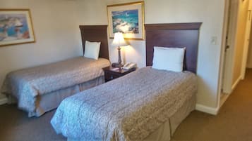 A hotel room with two single beds, a nightstand with a lamp, a painting on the wall, and a door to the right.