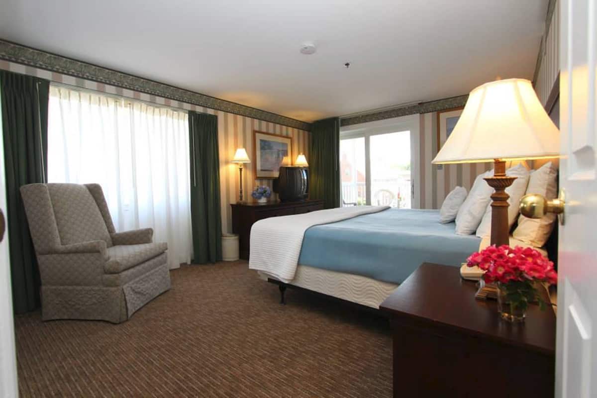 A hotel room with a bed, a chair, a desk, and a window with curtains.