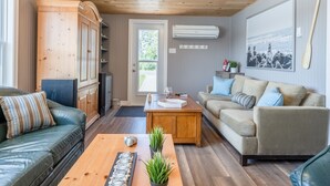A living room with a wooden ceiling, a beige sofa, a green sofa, a wooden coffee table, and a wooden cabinet. - Oceanfront Cottage on a Quiet Cove Just Outside Lunenburg (Lunenburg)