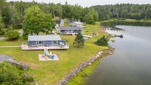 A lakeside lodge with a dock, outdoor seating, and a large tree. - Oceanfront Cottage on a Quiet Cove Just Outside Lunenburg (Lunenburg)