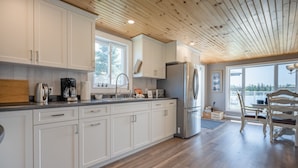 A modern kitchen with white cabinets, a stainless steel refrigerator, and a wooden ceiling. - Oceanfront Cottage on a Quiet Cove Just Outside Lunenburg (Lunenburg)