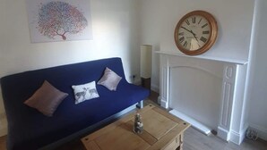 A living room with a blue sofa, a wooden coffee table, a wall-mounted clock, and a decorative wall piece. - Dartford RSG House (Dartford)