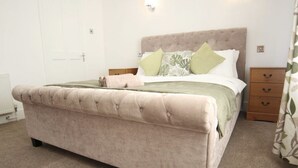 A bedroom with a tufted bed, a nightstand, and a wooden drawer unit. - Dartford RSG House (Dartford)