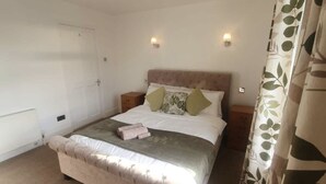 A bedroom with a large bed, two bedside tables, a radiator, and a curtain with a leaf pattern. - Dartford RSG House (Dartford)