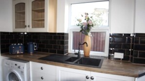 A kitchen with a washing machine, a sink, and a window with a vase of flowers. - Dartford RSG House (Dartford)