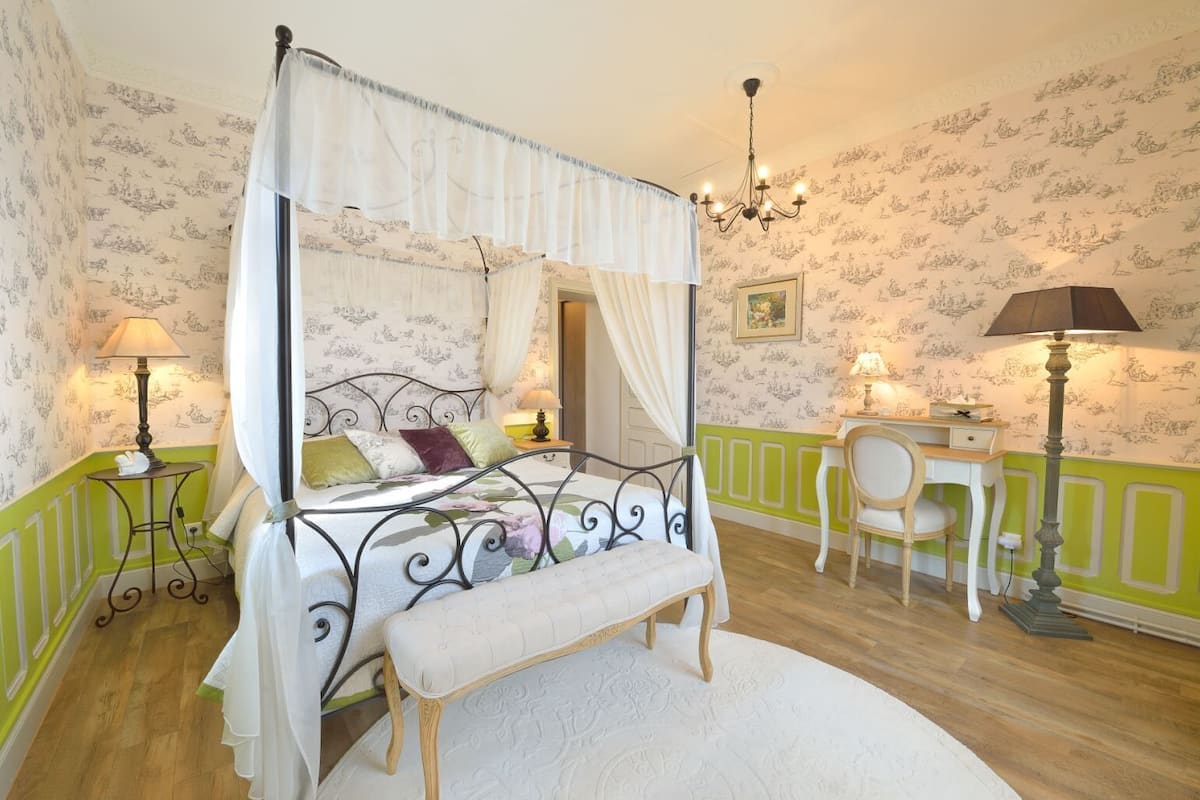 Ein Himmelbett mit Baldachin, ein Schreibtisch mit Stuhl und ein kleiner Tisch mit Lampe.