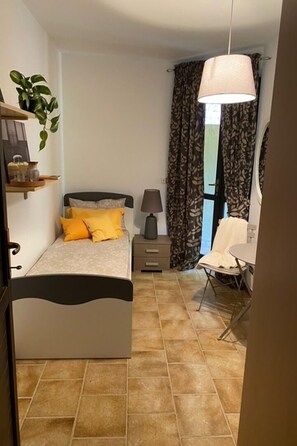 Cozy retreat with a single bed, nightstand, and potted plant.