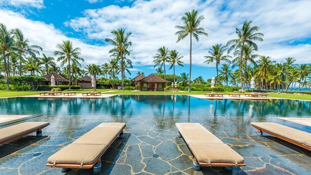 Ein Pool in einem Resort mit Liegestühlen, Palmen und blauem Himmel.