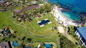 Eine Vogelperspektive zeigt ein Resort mit mehreren Schwimmbecken, einem Strand und einer felsigen Küstenlinie.