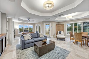 A spacious living room with a grey sofa, a wooden coffee table, and a dining area with wicker chairs. - At Sun Sea Terrace | Luxury Siesta Key Condo w/ Heated Pool, Short Walk to Beach and Village (Siesta Key)