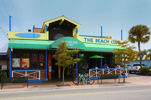 A beach club with a green and yellow exterior, a covered seating area, and a bicycle parked outside.