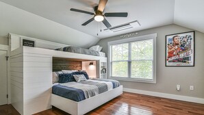 Un dormitorio con una cama litera, ventilador de techo, ventana grande con persianas y un cartel en la pared.