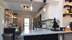 A modern kitchen with granite countertops, black bar stools, and pendant lighting.