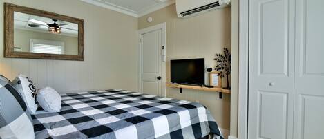 A bedroom with a checkered bedspread, a ceiling fan, a mounted TV, and a wardrobe.