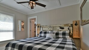A bedroom with a checkered bedspread, a ceiling fan, a wooden headboard, and a mirror on the wall.