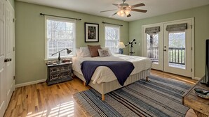 Une chambre à coucher comprenant un lit, une table de chevet, un bureau, un ventilateur de plafond et une vue sur l’extérieur par une porte.