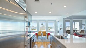 A modern kitchen with stainless steel appliances, wooden flooring, and a dining area with a view.