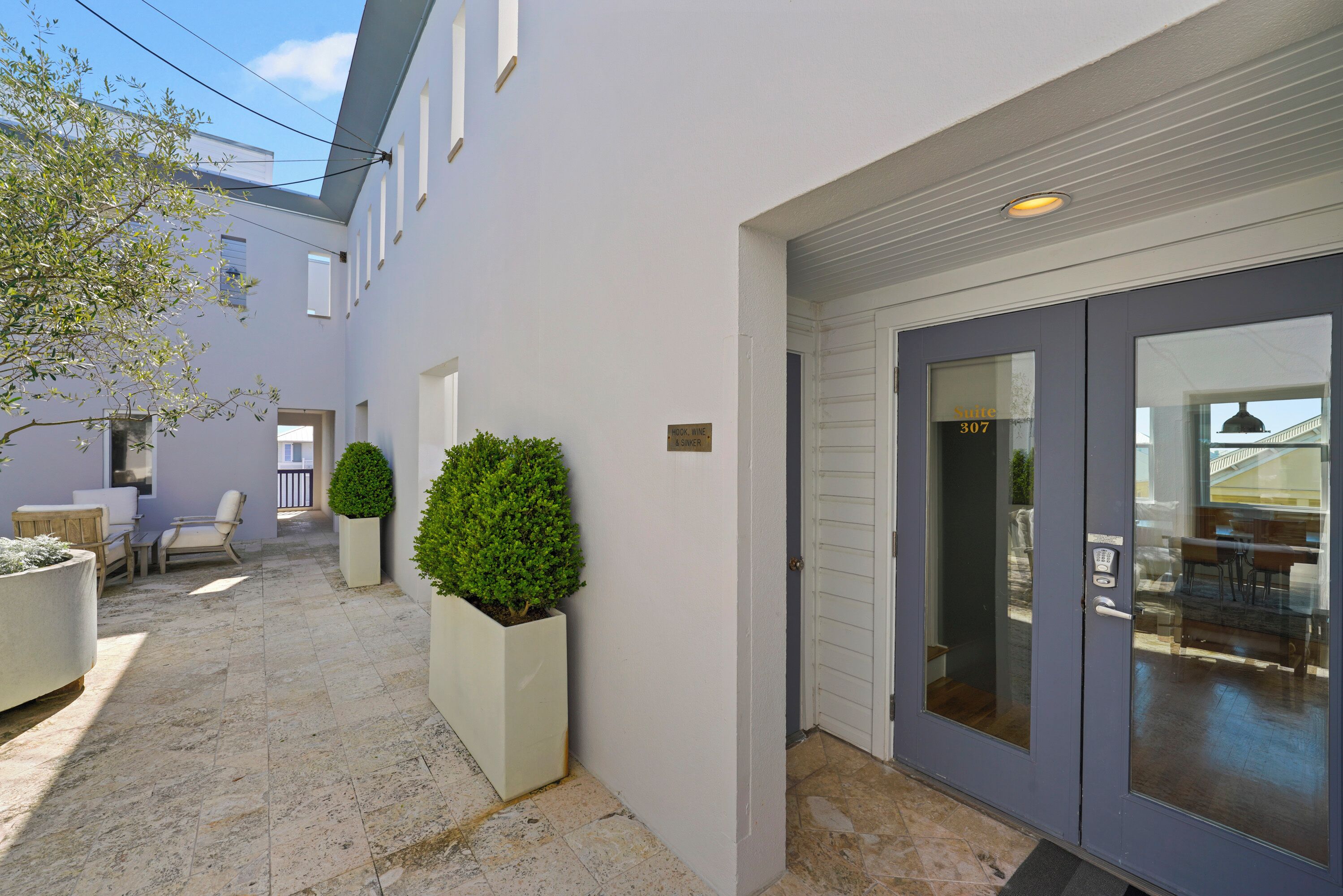 A modern building exterior with a garage door, a small patio area with seating, and potted plants.