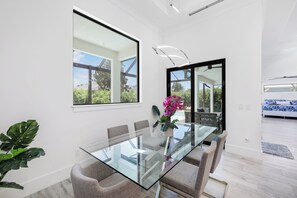 A modern dining area with a glass table, cushioned chairs, and a potted plant. - Modern Home | Pool & Steps to Beach, Food & Fun (Marco Island)