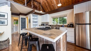 A modern kitchen with a large island, stainless steel appliances, and a wooden ceiling. - Private Country Cottage | 2+ Bedroom on 1-acre | 5 mins to Kamuela town (Waimea)