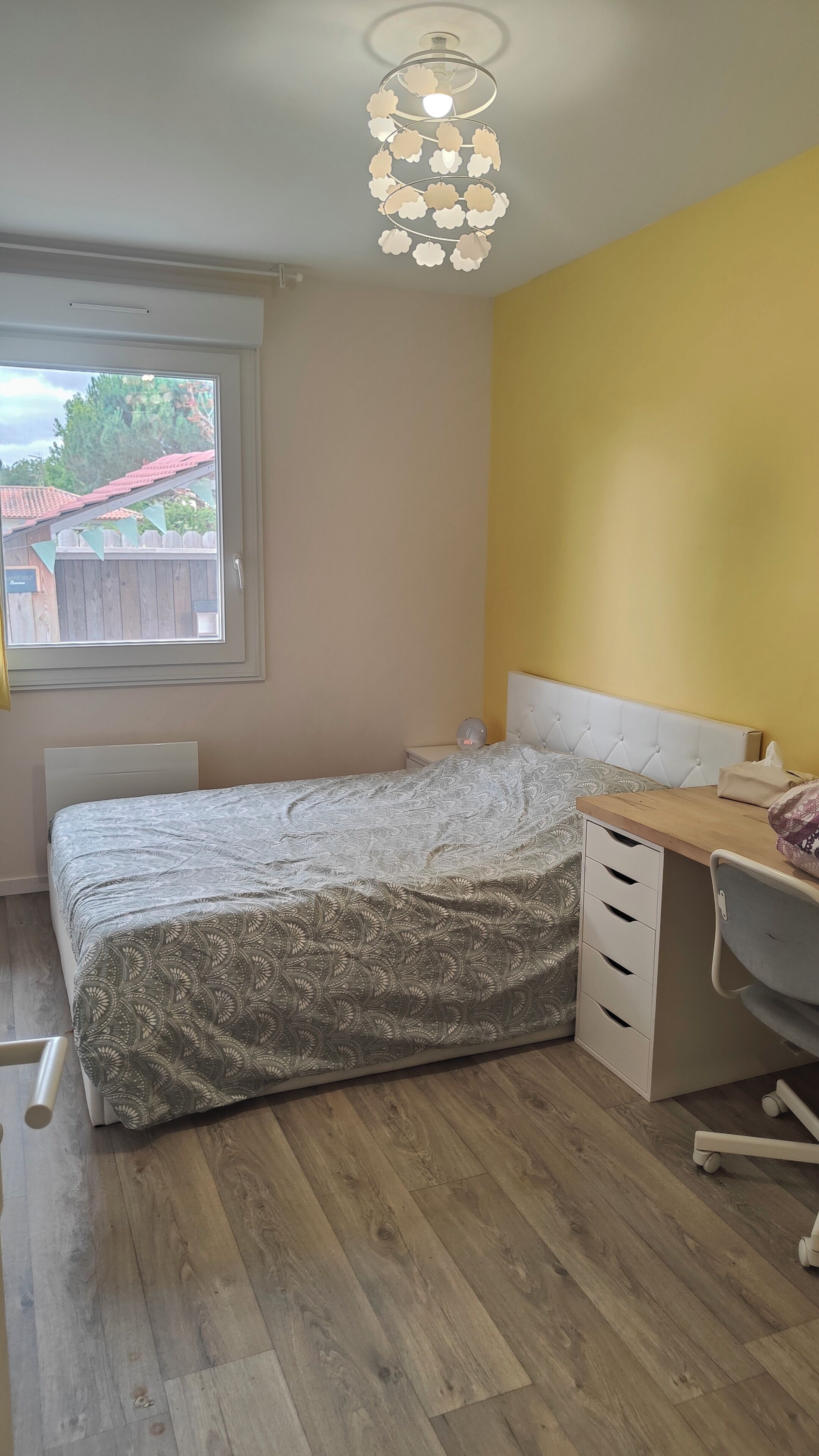 Ein Schlafzimmer mit Bett, Schreibtisch und Stuhl. Ein Fenster bietet Blick auf ein Gebäude.