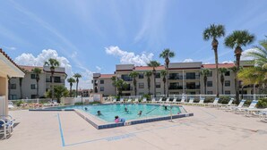 Un área de piscina con varias piscinas, palmeras y un edificio de techo con tejas rojas.