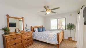Un dormitorio con una cama de madera, un aparador, un ventilador de techo, una ventana con persianas y una planta en maceta.