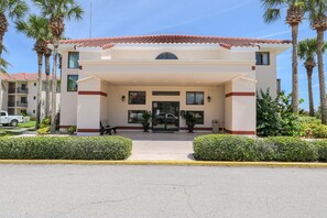A hotel entrance with a covered walkway, palm trees, and a vehicle parked outside.