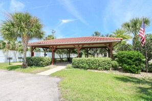 A covered pavilion with a tiled roof, surrounded by greenery and a flag.
