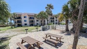 Un patio con mesas de picnic y palmeras, rodeado por un edificio con varios balcones.