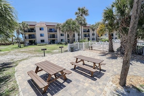 A courtyard with picnic tables and palm trees, surrounded by a building with multiple balconies.