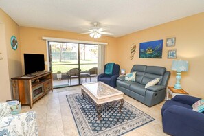 A living room with a television, sofa, coffee table, and a view through a sliding door to an outdoor area.