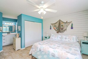 Un dormitorio con cama, ventilador de techo, un adorno en la pared y ventana con persianas.