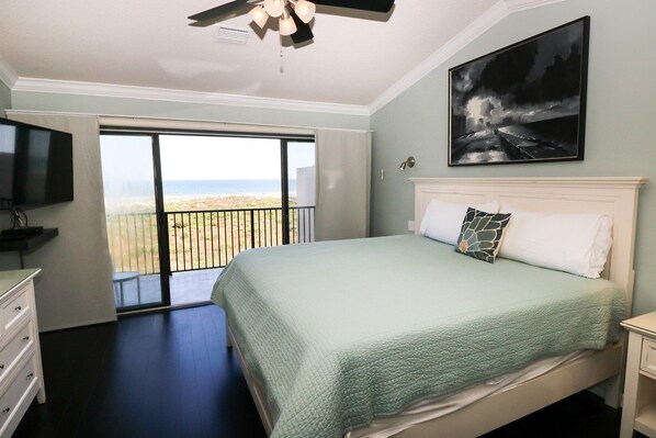A bedroom with a bed, a TV, a painting, and a balcony with a view.