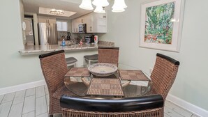 A dining area with wicker chairs, a glass table, and a kitchen in the background.