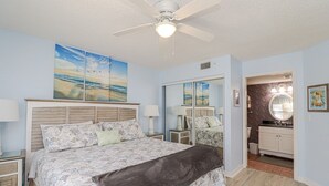 A bedroom with a large bed, a ceiling fan, and a bathroom with a vanity and mirror. - Ocean Village Club Condo R28 (St. Augustine)