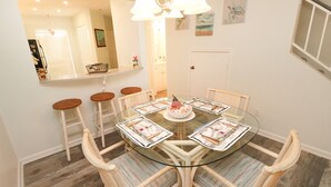 Een eetgedeelte met een glazen tafel, rieten stoelen en een witte deur op de achtergrond.
