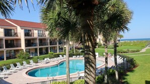 Een resort met een zwembad, ligbedden, palmbomen en uitzicht op de oceaan.