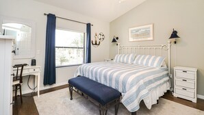 Ein Schlafzimmer mit einem Bett, einem Schreibtisch, einem Stuhl, einer Bank, einem Nachttisch und einem Deckenventilator.