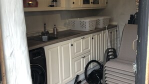 A compact kitchen with a washing machine, a sink, and a chair. - The Inn at Glencairn (Lismore)