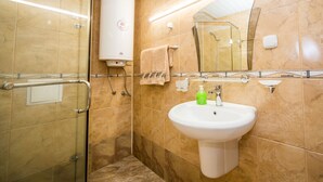 Een badkamer met een douchecabine van glas, een wit wastafelmeubel met een groene zeepdispenser en een handdoekrek.
