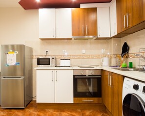 Cocina compacta con refrigerador de acero inoxidable, microondas, tostadora, horno y lavadora.