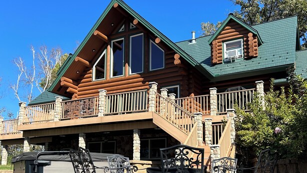 A log cabin with a balcony, outdoor seating, and a covered barbecue area.