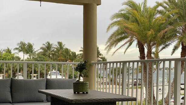 A balcony with wicker furniture, a potted plant, and a view of the marina. - Waterfront condo overlooking Palm Beach (West Palm Beach)