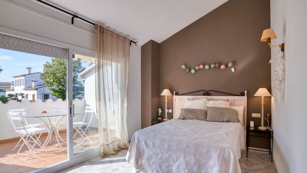 Une chambre dotée d’un grand lit, de deux tables de chevet avec des lampes, d’une porte vitrée donnant sur un balcon avec des chaises, et d’un élément décoratif fixé au mur.