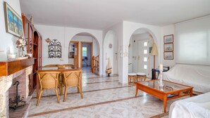Un salon spacieux doté d’une cheminée, un coin repas avec des meubles en osier et un espace salon confortable avec un canapé et une table basse.