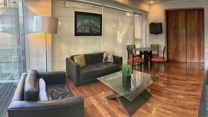 A modern living room with a glass coffee table, leather sofa, and a dining area with red chairs. - Aura For Living (Mexico City)