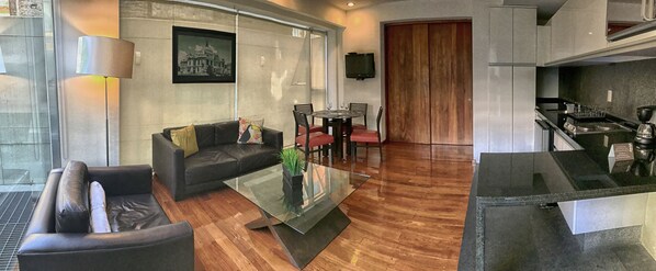 A modern living room with a glass coffee table, leather sofa, and a dining area with red chairs.