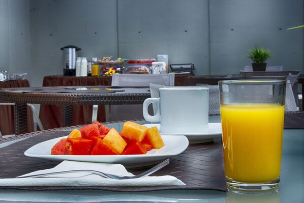 Disposição para o café da manhã com uma tábua de frutas, um copo de suco de laranja e uma xícara de café em uma mesa.